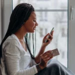 امرأة تستخدم هاتفها وبطاقتها البنكية في المنزل - البنوك الرقمية بدون رسوم في كندا